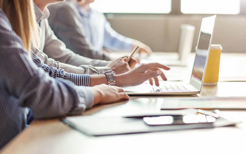 Menschen sitzen am Schreibtisch und tippen am Laptop